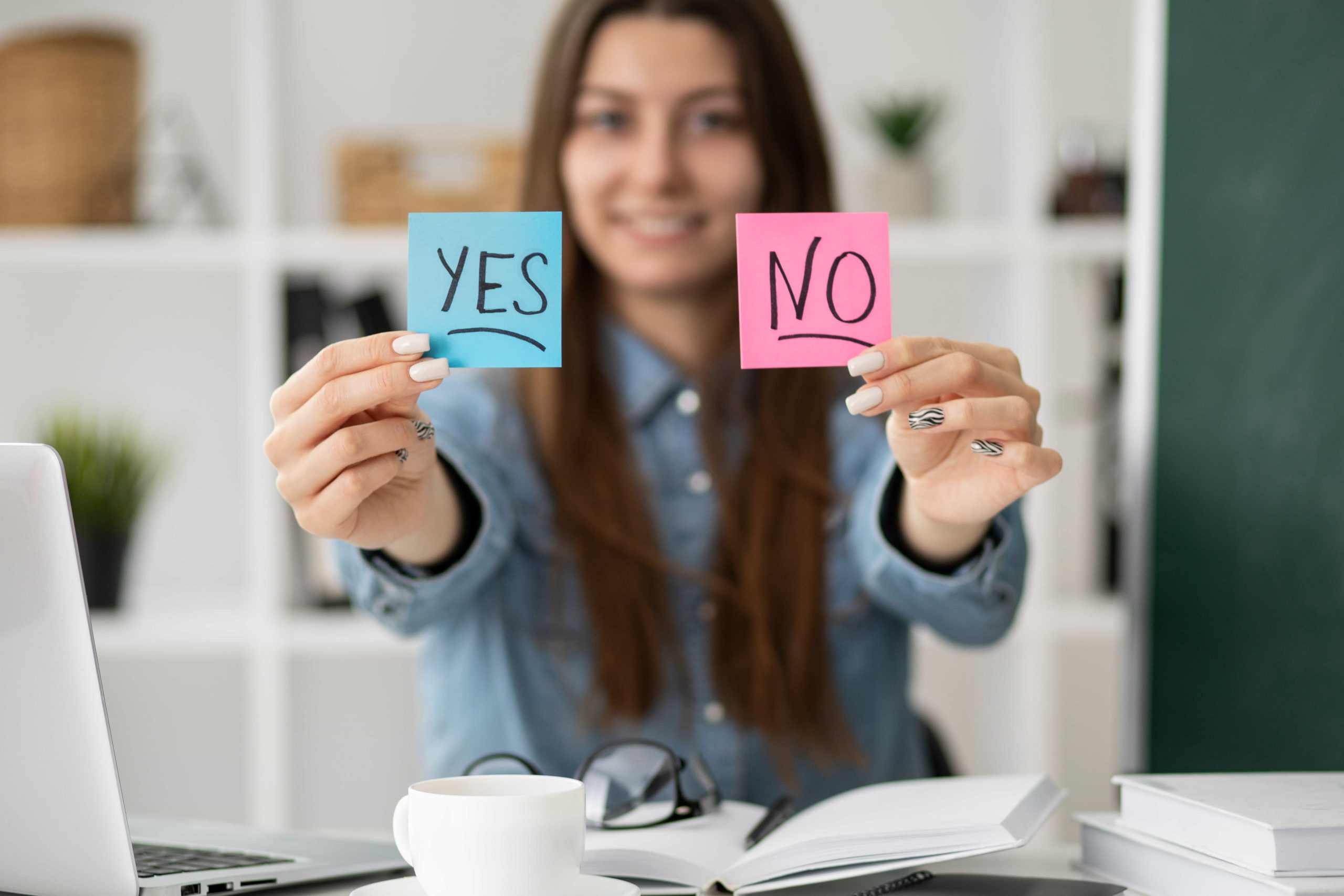Una chica frente a un escritorio con un post-it en cada mano. Uno dice yes y el otro no.
